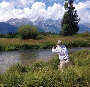 back view of man casting into water with mountains in background